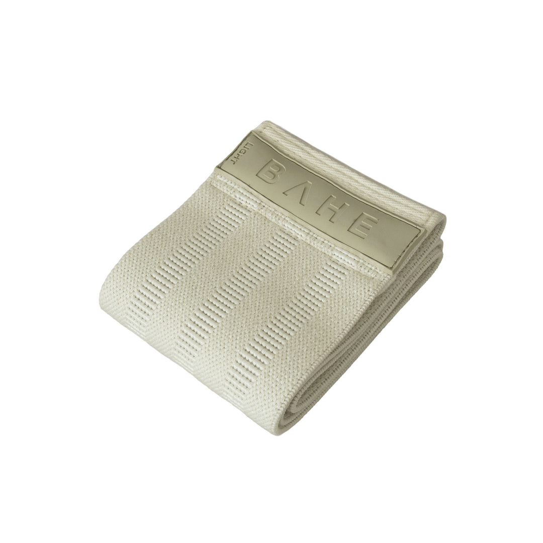 A folded beige textured booty band with beige end tab embossed with the brand name &