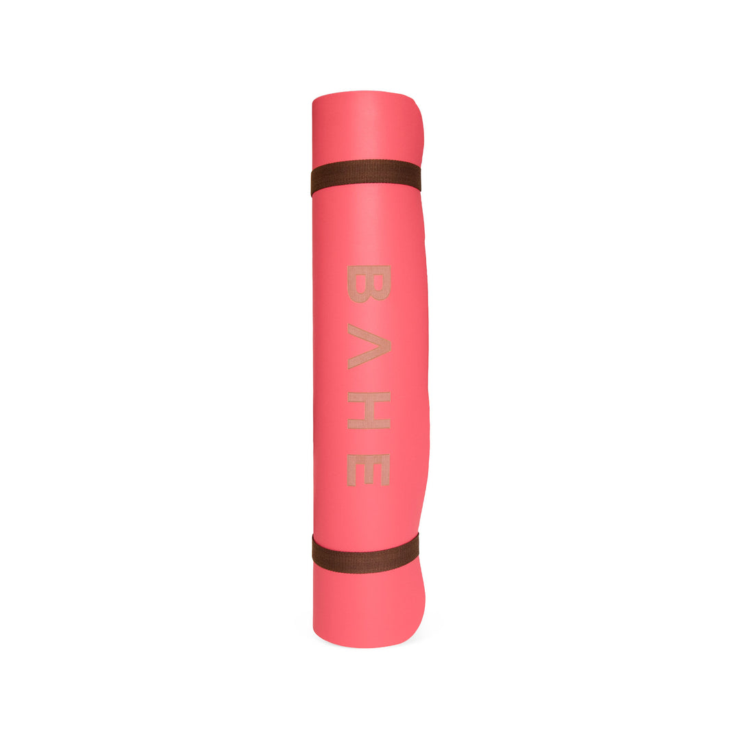Pink yoga mat with brown accents on a white background